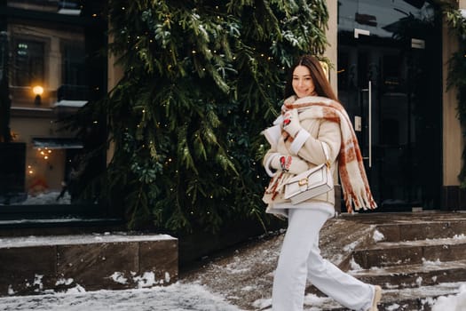 A girl with long hair in a scarf and with a white handbag walks down the street in winter.