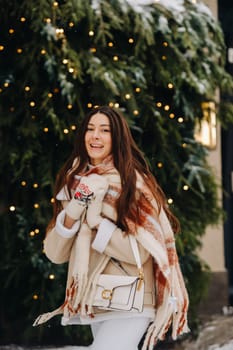 A girl with long hair in a scarf and with a white handbag walks down the street in winter.