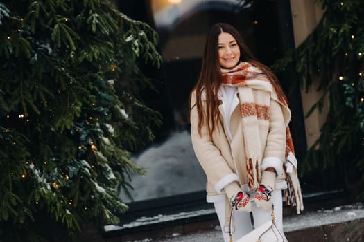 A girl with long hair in a scarf and with a white handbag walks down the street in winter.