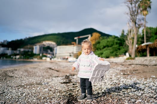 Little girl carries a piece of styrofoam on a pebbly beach. High quality photo