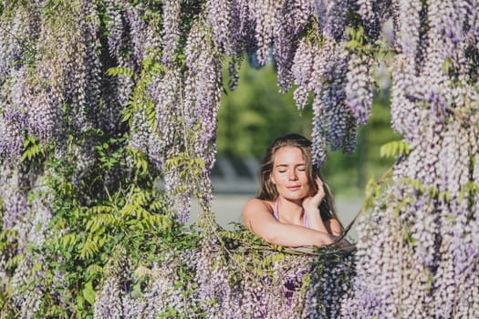 Woman wisteria lilac dress. Thoughtful happy mature woman in purple dress surrounded by chinese wisteria.