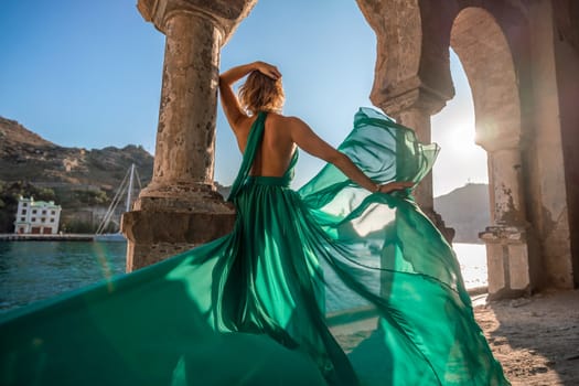 Woman dress sea columns. Rear view of a happy blonde woman in a long mint dress posing against the backdrop of the sea in an old building with columns