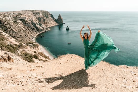 Woman green dress sea. Female dancer posing on a rocky outcrop high above the sea. Girl on the nature on blue sky background. Fashion photo