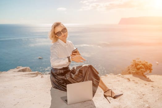 Freelance women sea. She is working on the computer. Good looking middle aged woman typing on a laptop keyboard outdoors with a beautiful sea view. The concept of remote work