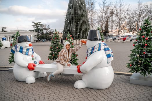 Woman Christmas Square. Close-up of a winter white toy snowman With trees decorated with Christmas tinsel in the background.