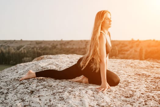 Well looking middle aged woman with long hair, fitness instructor in leggings and tops doing stretching and pilates on the rock near forest. Female fitness yoga routine concept. Healthy lifestyle.