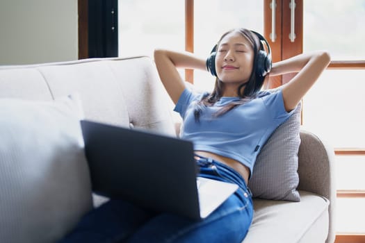 woman wearing headphones on comfortable couch listening to using computer laptop and music