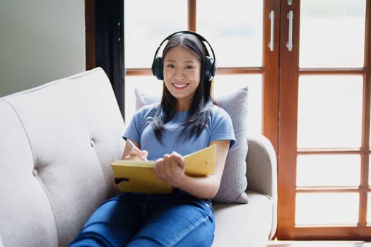 woman wearing headphones to listen music and reading notebook on sofa