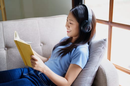 woman wearing headphones to listen music and reading notebook on sofa