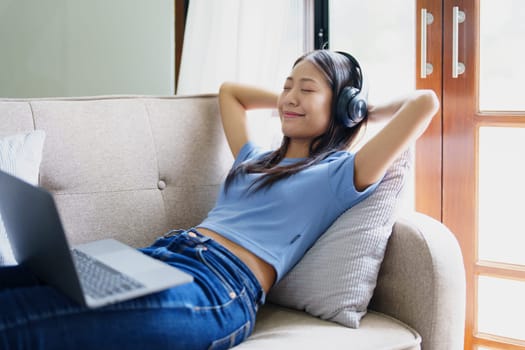 woman wearing headphones on comfortable couch listening to using computer laptop and music