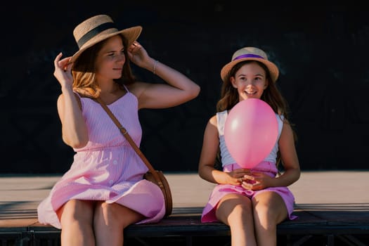 mother and daughter are sitting in pink dresses with flowing long hair on a black background. Enjoy communicating with each other.