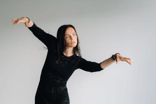 A girl in a black dress moves in a dance on a gray background. Dynamic dance,