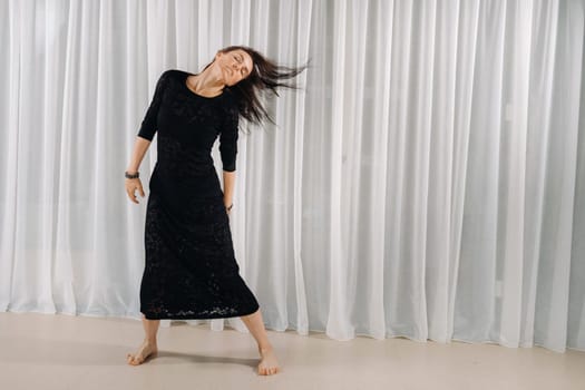 A girl in a black dress moves in a dance on a gray background. Dynamic dance,