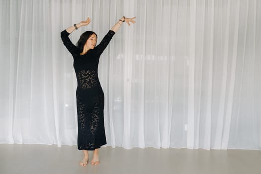 A girl in a black dress moves in a dance on a gray background. Dynamic dance,