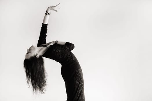 A girl in a black dress moves in a dance on a gray background. Dynamic dance,