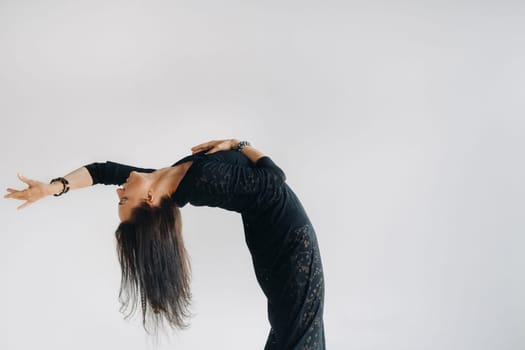 A girl in a black dress moves in a dance on a gray background. Dynamic dance,