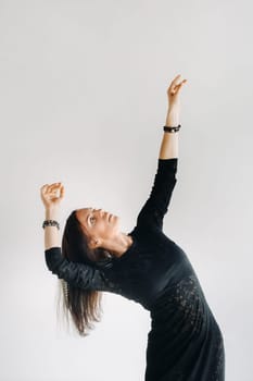 A girl in a black dress moves in a dance on a gray background. Dynamic dance,