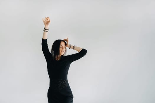 A girl in a black dress moves in a dance on a gray background. Dynamic dance,