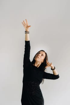 A girl in a black dress moves in a dance on a gray background. Dynamic dance,