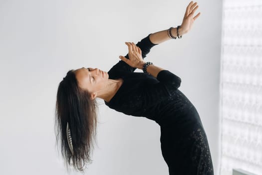 A girl in a black dress moves in a dance on a gray background. Dynamic dance,