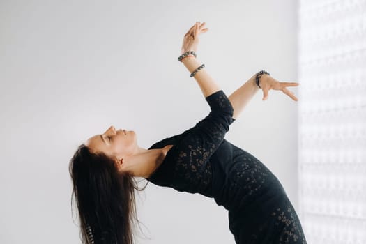 A girl in a black dress moves in a dance on a gray background. Dynamic dance,