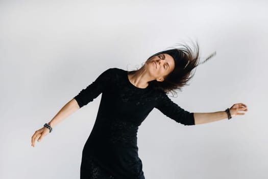 A girl in a black dress moves in a dance on a gray background. Dynamic dance,