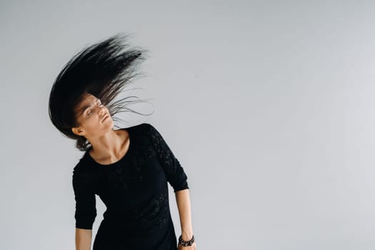 A girl in a black dress moves in a dance on a gray background. Dynamic dance,