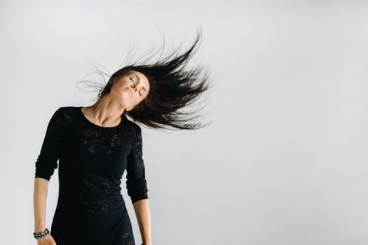 A girl in a black dress moves in a dance on a gray background. Dynamic dance,