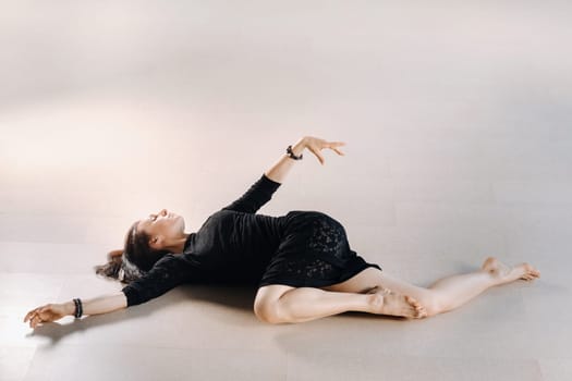 A girl in a black dress lying down moves in a dance on the floor. Dynamic dance.