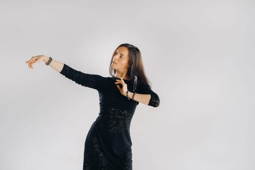 A girl in a black dress moves in a dance on a gray background. Dynamic dance,