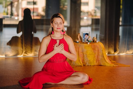 Meditation and concentration. a woman in a red dress, sitting on the floor with her eyes closed, is practicing medicine indoors. Peace and relaxation.