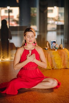 Meditation and concentration. a woman in a red dress, sitting on the floor with her eyes closed, is practicing medicine indoors. Peace and relaxation.