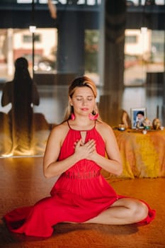 Meditation and concentration. a woman in a red dress, sitting on the floor with her eyes closed, is practicing medicine indoors. Peace and relaxation.