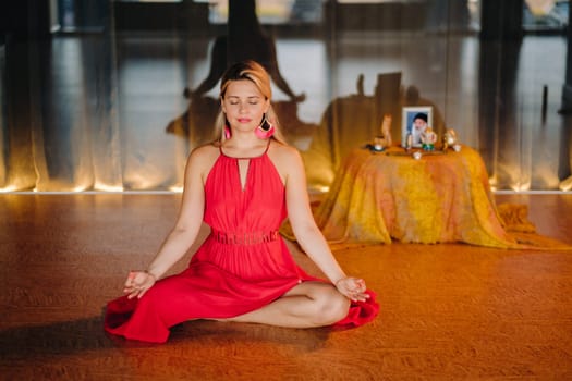 Meditation and concentration. a woman in a red dress, sitting on the floor with her eyes closed, is practicing medicine indoors. Peace and relaxation.