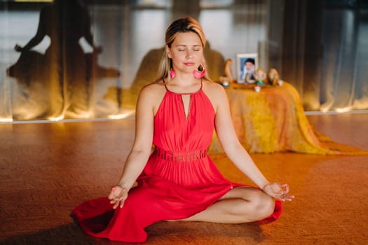 Meditation and concentration. a woman in a red dress, sitting on the floor with her eyes closed, is practicing medicine indoors. Peace and relaxation.