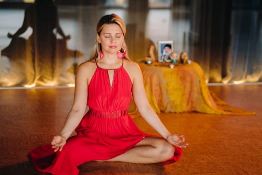 Meditation and concentration. a woman in a red dress, sitting on the floor with her eyes closed, is practicing medicine indoors. Peace and relaxation.