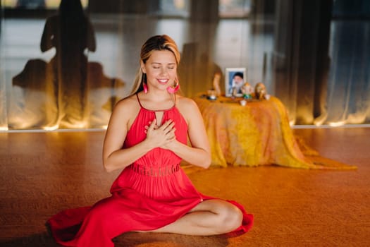 Meditation and concentration. a woman in a red dress, sitting on the floor with her eyes closed, is practicing medicine indoors. Peace and relaxation.