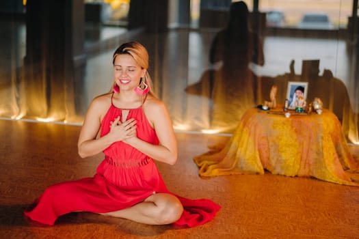 Meditation and concentration. a woman in a red dress, sitting on the floor with her eyes closed, is practicing medicine indoors. Peace and relaxation.