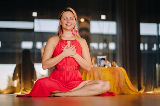 Meditation and concentration. a woman in a red dress, sitting on the floor with her eyes closed, is practicing medicine indoors. Peace and relaxation.