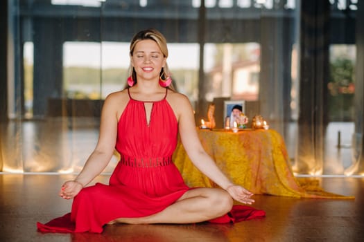 Meditation and concentration. a woman in a red dress, sitting on the floor with her eyes closed, is practicing medicine indoors. Peace and relaxation.