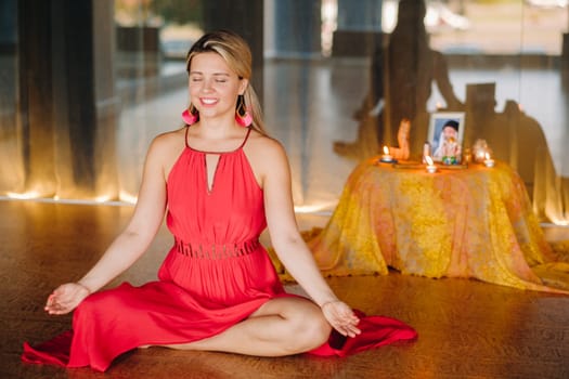 Meditation and concentration. a woman in a red dress, sitting on the floor with her eyes closed, is practicing medicine indoors. Peace and relaxation.