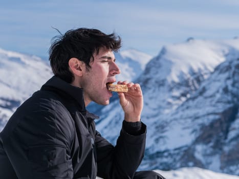 A man sitting on top of a snow covered mountain eating a piece of food