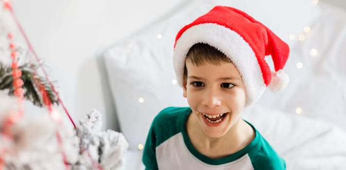 Portrait of cheerful boy smiling and laughing next to Christmas tree at house. Families and children generation alpha celebrating winter holidays.