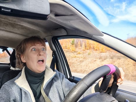 Terrified female driver a second before the accident. Scared middle-aged adult woman holds the steering wheel of car. Frightened Lady girl who is owner or rent a car for travel