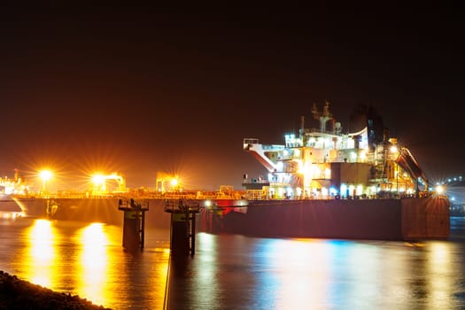 Majestic view of the Rotterdam port at night, shrouded in mist with the city lights illuminating the surroundings, creating a captivating and atmospheric scene.