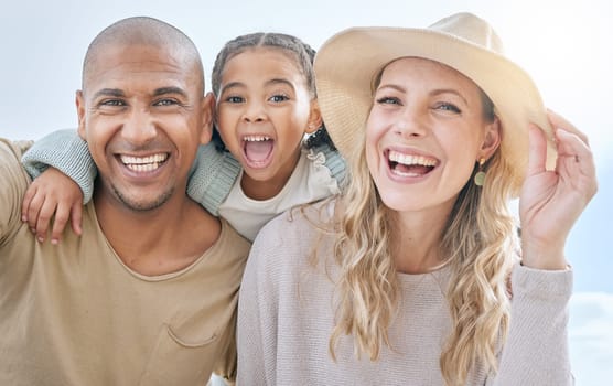Summer, blue sky and portrait of young family having fun, laugh and play together. Multicultural mom, dad and girl outdoors on beach holiday and vacation. Love, bonding and couple with kid on weekend.