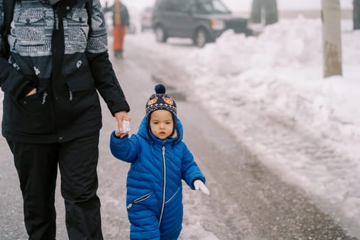 Little girl walks holding her mother hand along a snowy road. Cropped. High quality photo