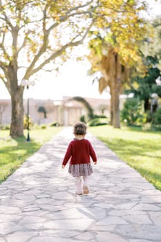 Little girl walks along a paved path in the park looking at her feet. High quality photo