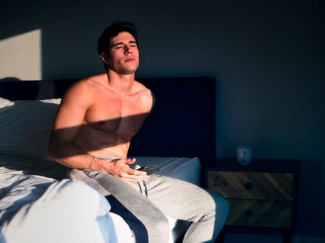A shirtless man sitting on a bed in a bedroom