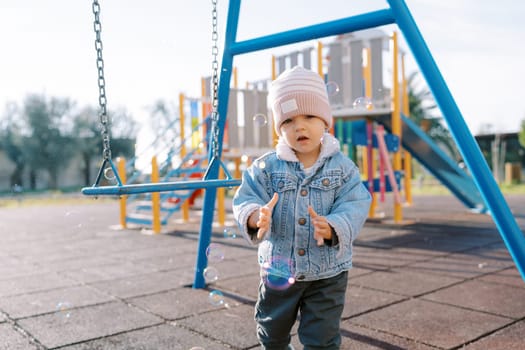 Little girl catches soap bubbles near the swing. High quality photo